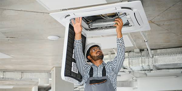 Technician inspecting a ceiling-mounted air conditioning and airflow unit